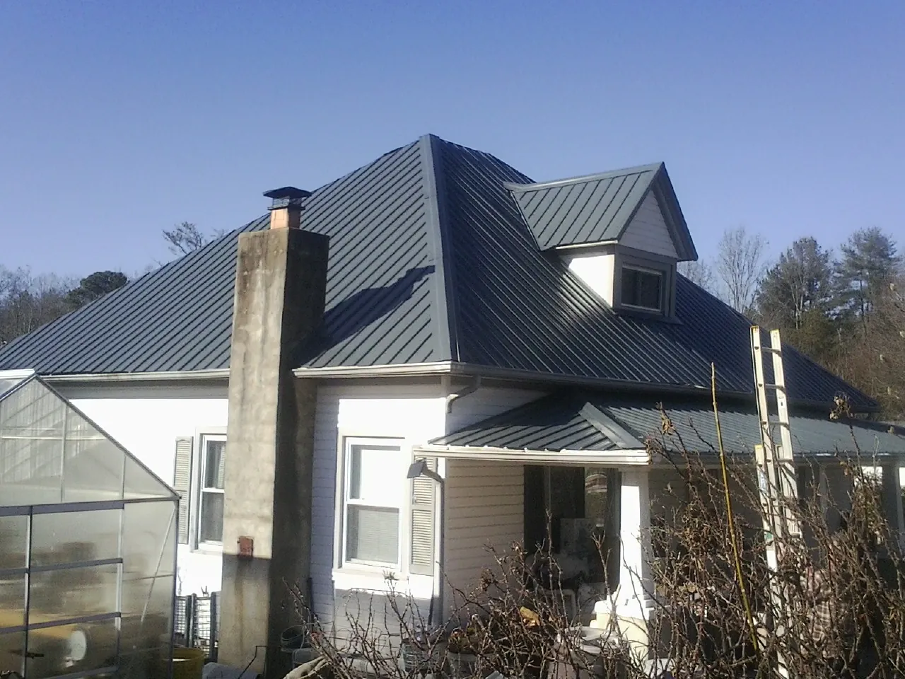 Dark blue standing seam metal roof on a white farmhouse with dormer — Slate & Tile Roof Repair by Roofing Brothers in Kempner
