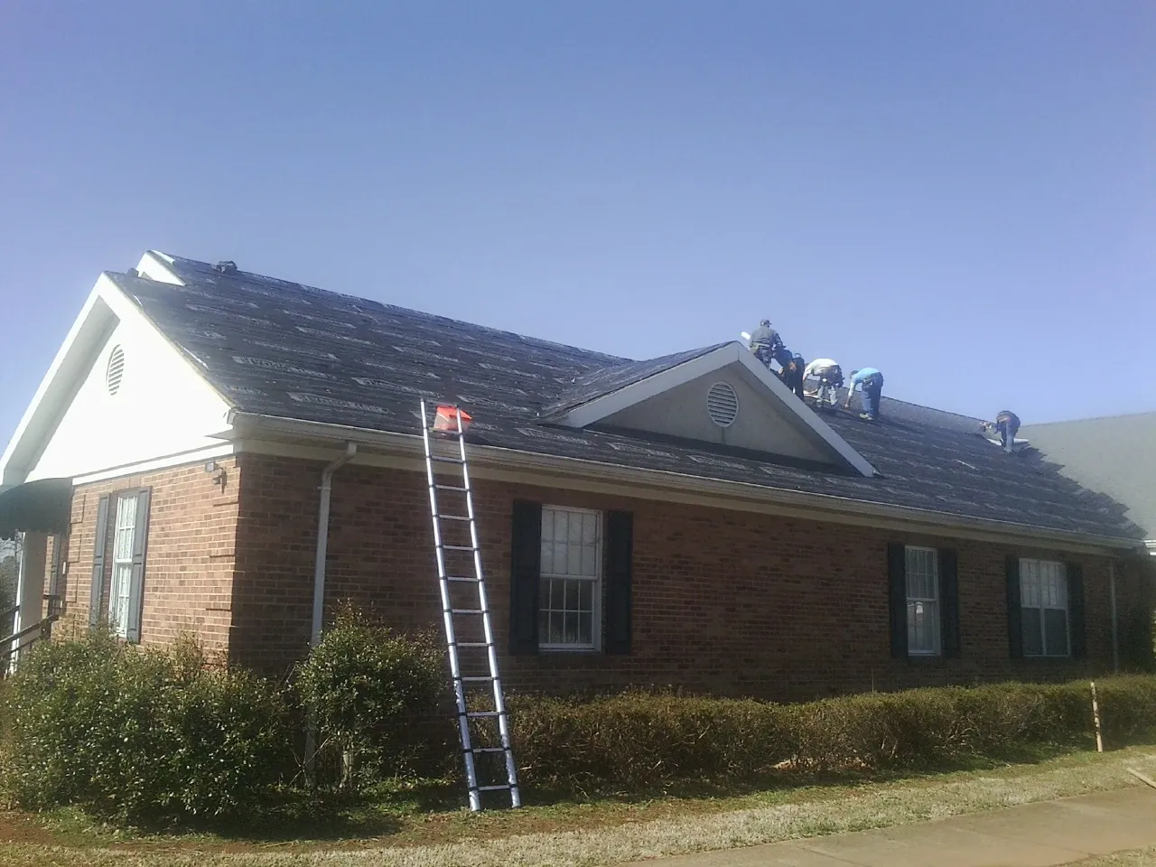 Crew tearing shingles off a brick ranch roof with a ladder set — Metal Roof Repair work by our crew in Kempner