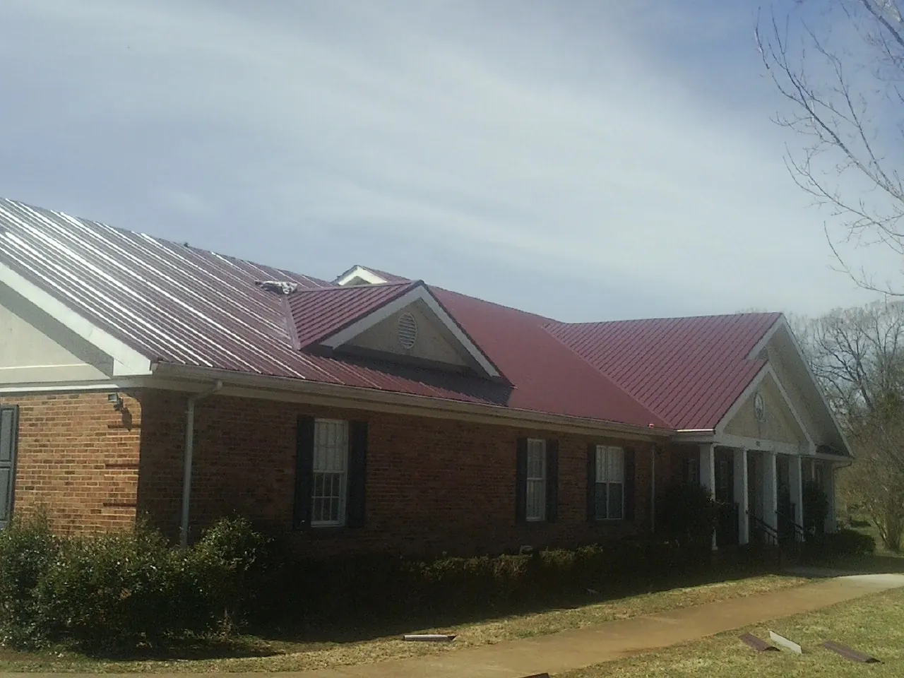 Red metal roof with gabled entries on a long brick building, from a Hail Damage Roof Repair job in Kempner