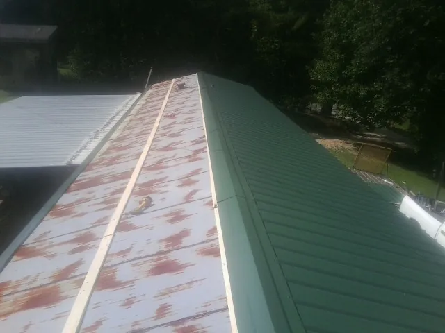Old rusted panels beside newly installed green metal roofing — Wind Damage Roof Repair by Roofing Brothers in Kempner
