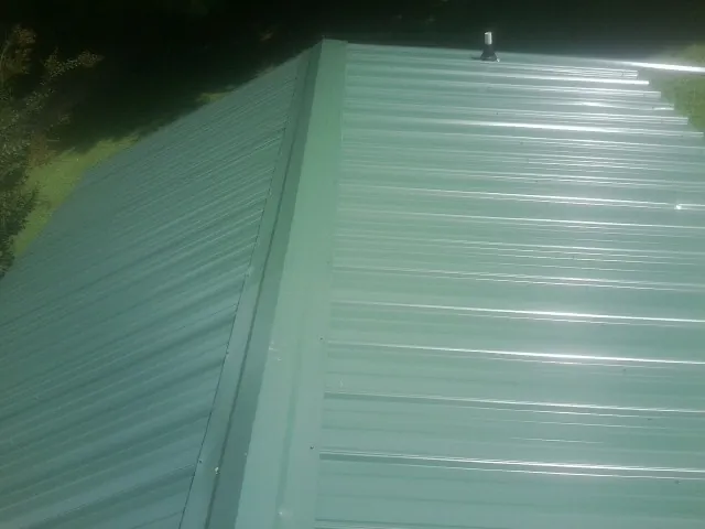 New green metal panels meeting at the ridge of a roof — Flat Roof Repair work by our crew in Kempner