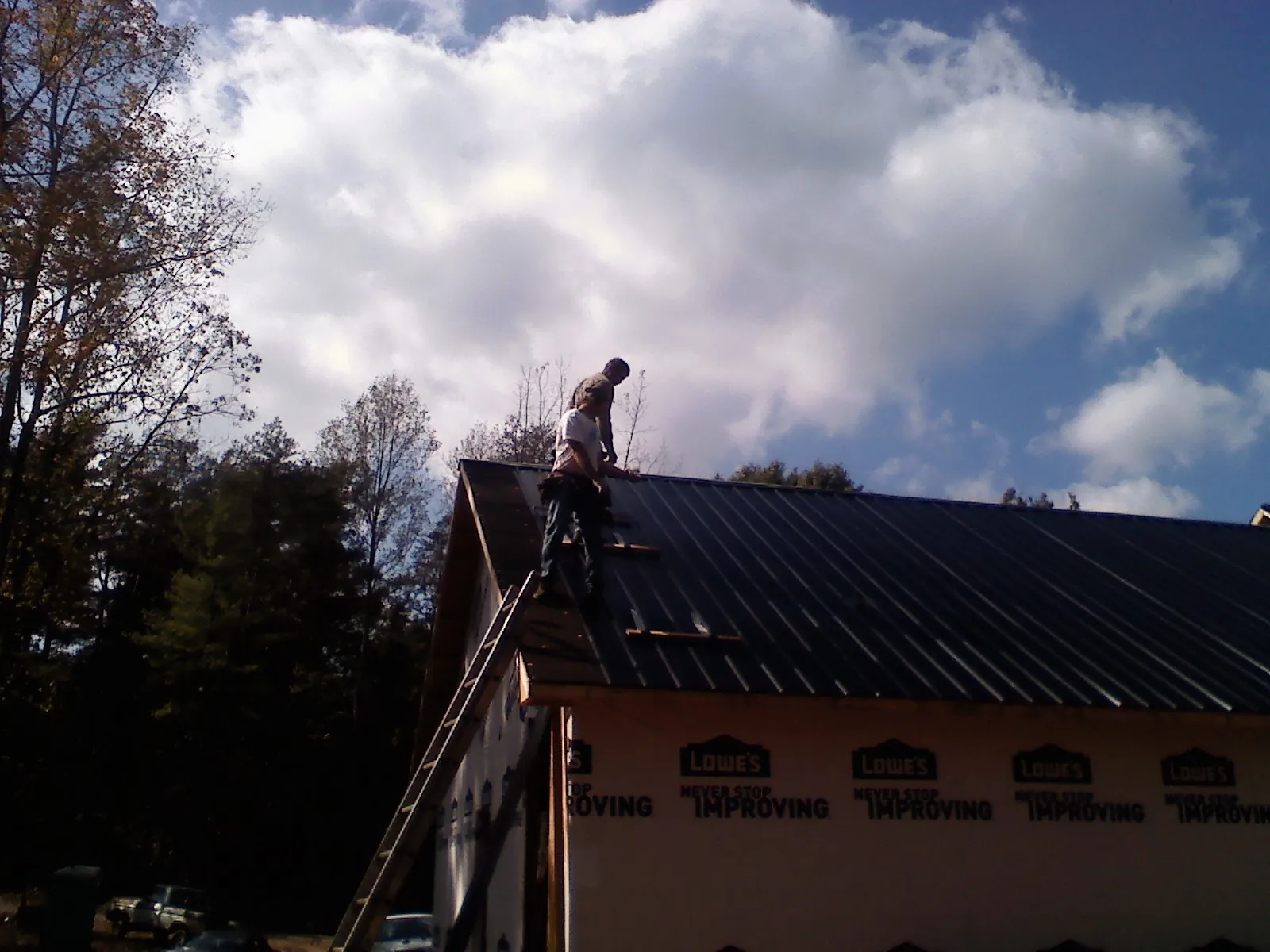Roofer fastening dark metal panels high against a cloudy sky, from a Roof Inspection job in Kempner