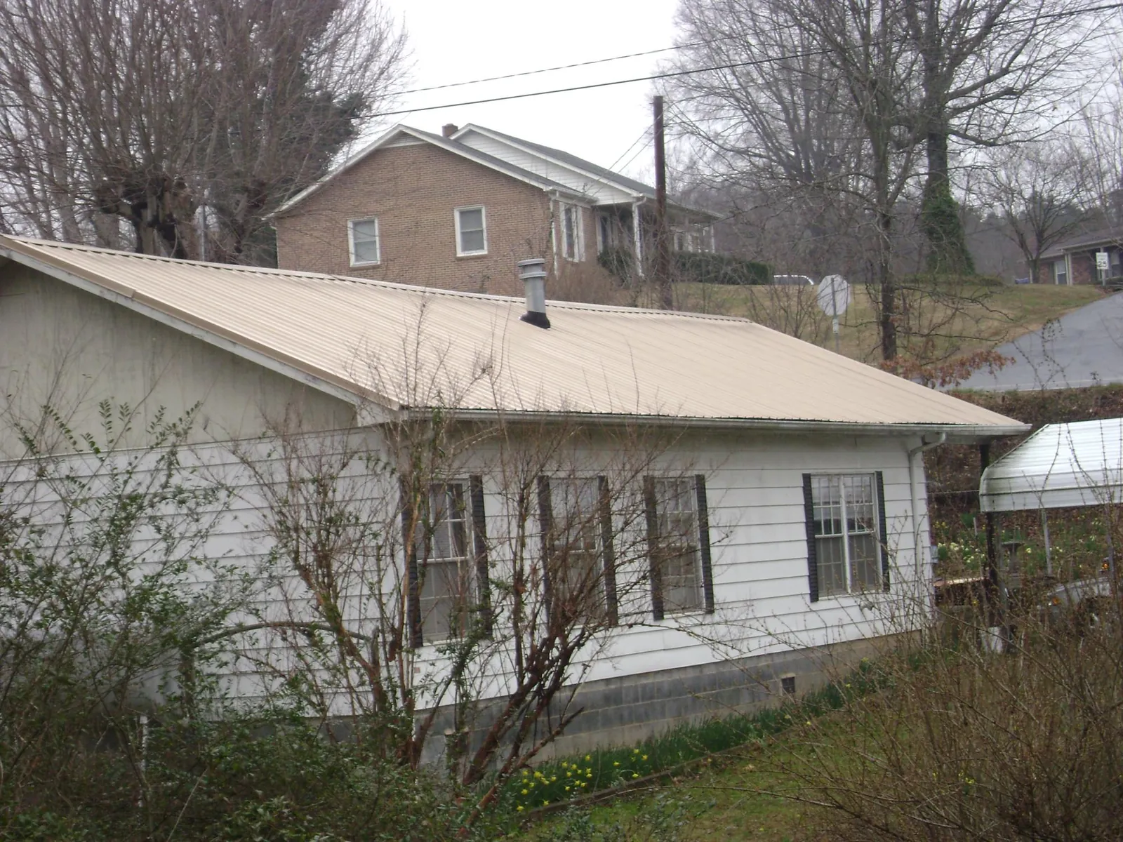 Tan metal roof on a white sided house set into a hillside — Commercial Roofing by Roofing Brothers in Kempner